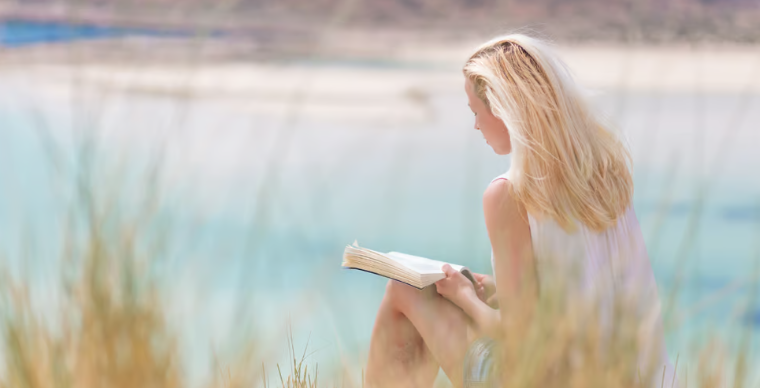 Woman reading a book near reeds and a lake