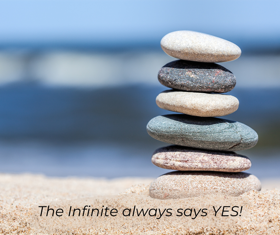 Stacked rocks on sand at the beach. Text: The Infinite always says YES!